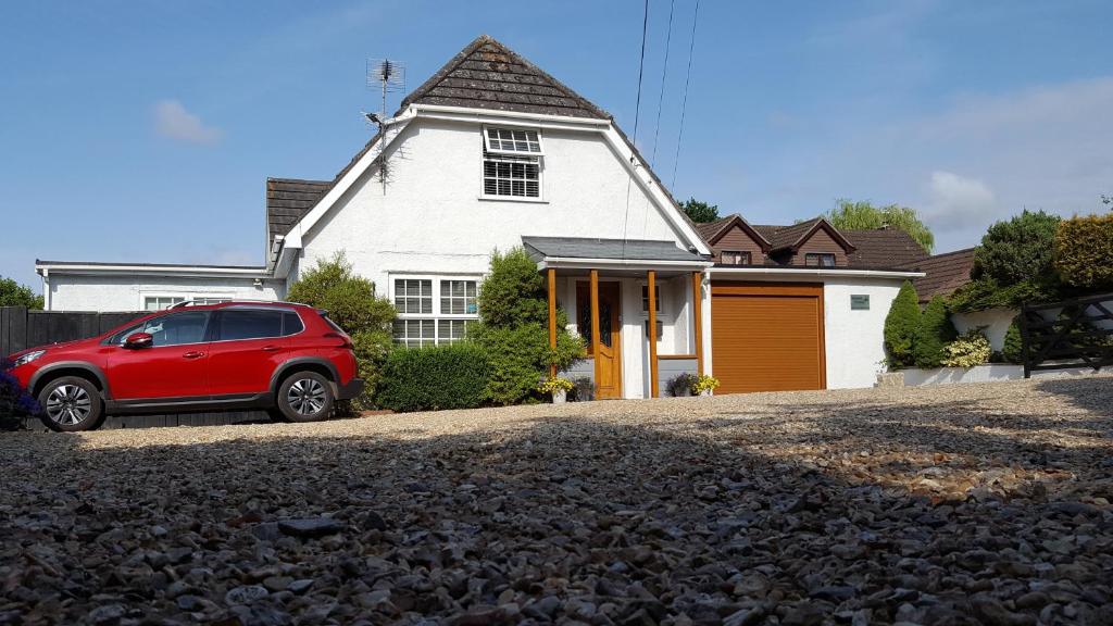 un coche rojo estacionado frente a una casa blanca en Canford Crossing, en Wimborne Minster