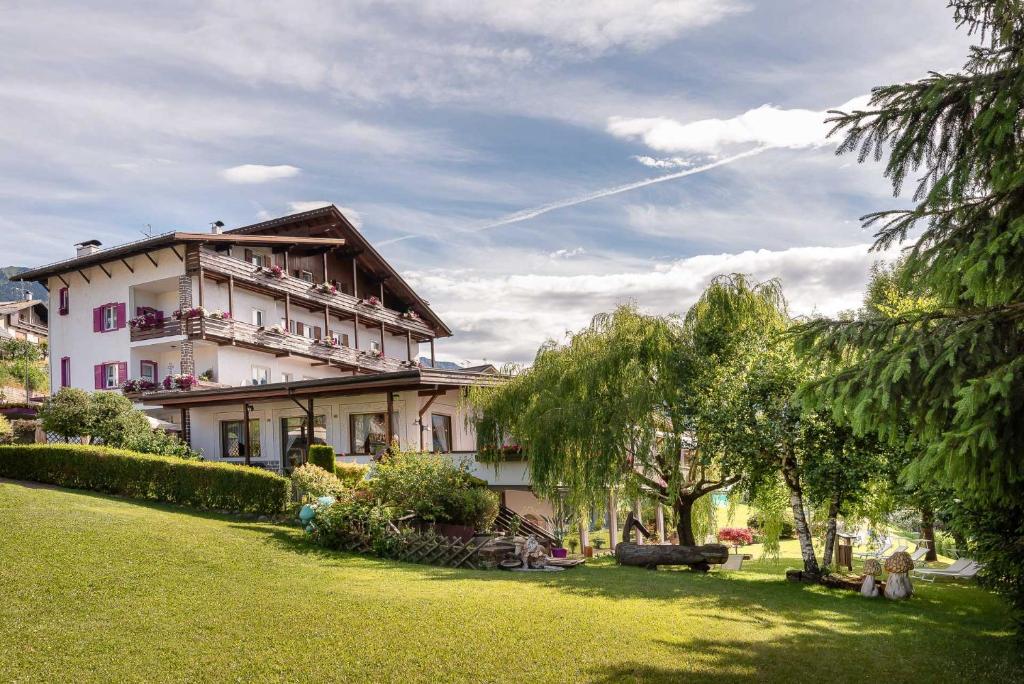 ein großes weißes Gebäude in einem Hof mit Bäumen in der Unterkunft Hotel Latemar in Castello di Fiemme