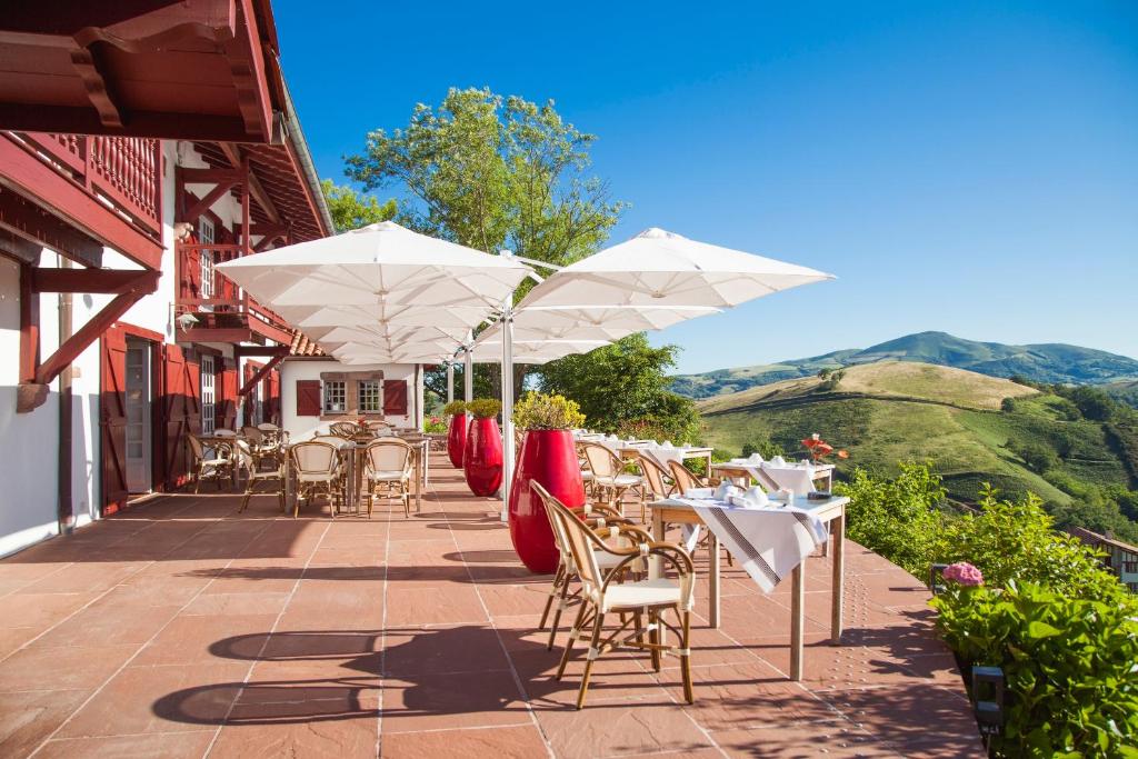 un patio con mesas, sillas y sombrillas blancas en Auberge Ostapé en Bidarray