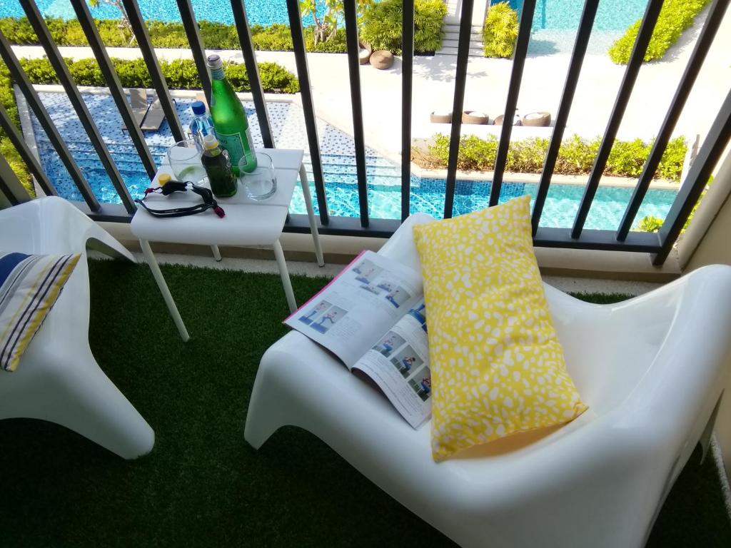 a balcony with a white chair with a book and a table at Rain​ Cha​ Am​ -​ Hua​ ​Hin​ by​ Good​ Luck​ Home in Cha Am