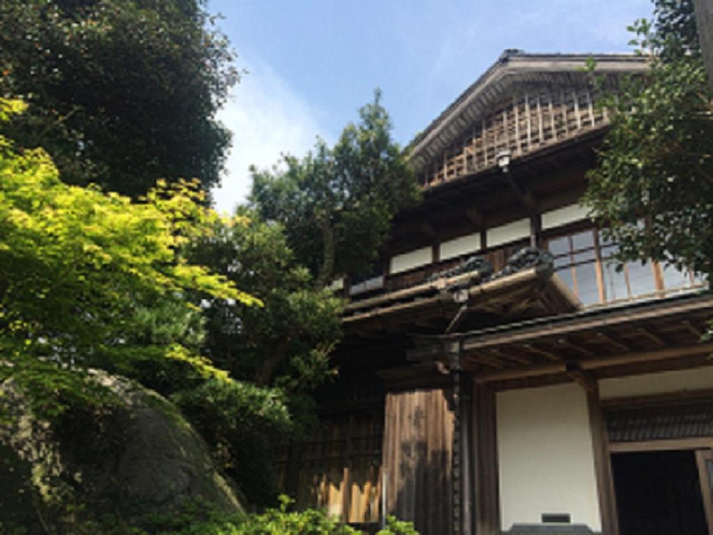 un vieux bâtiment avec des arbres devant lui dans l'établissement 里や, à Itoshima