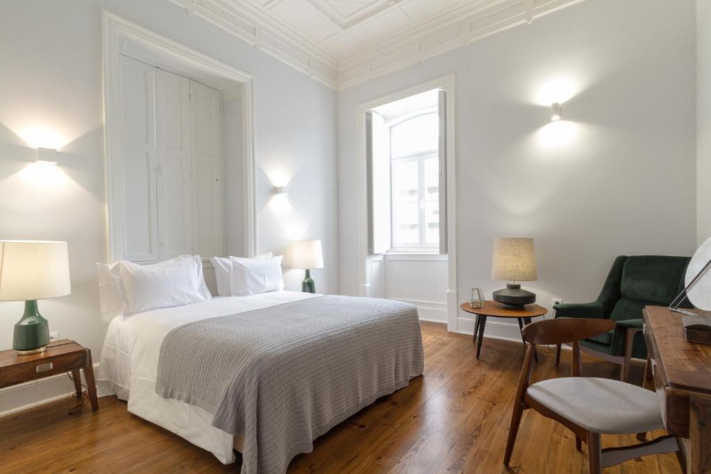 a white bedroom with a bed and a chair at AQ 188 Guest House in Coimbra