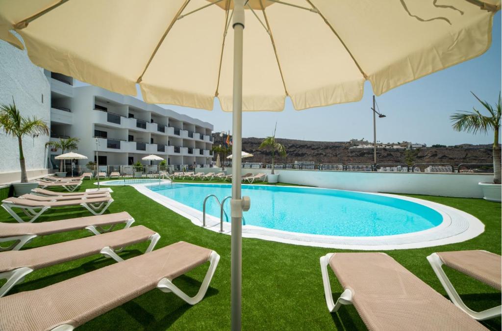 a swimming pool with lounge chairs and an umbrella at Montesol Atsol in Puerto Rico de Gran Canaria