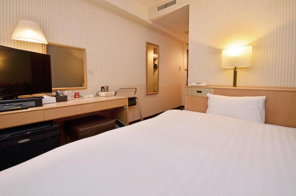 um quarto de hotel com uma cama grande e uma televisão em Omura Central Hotel em Omura