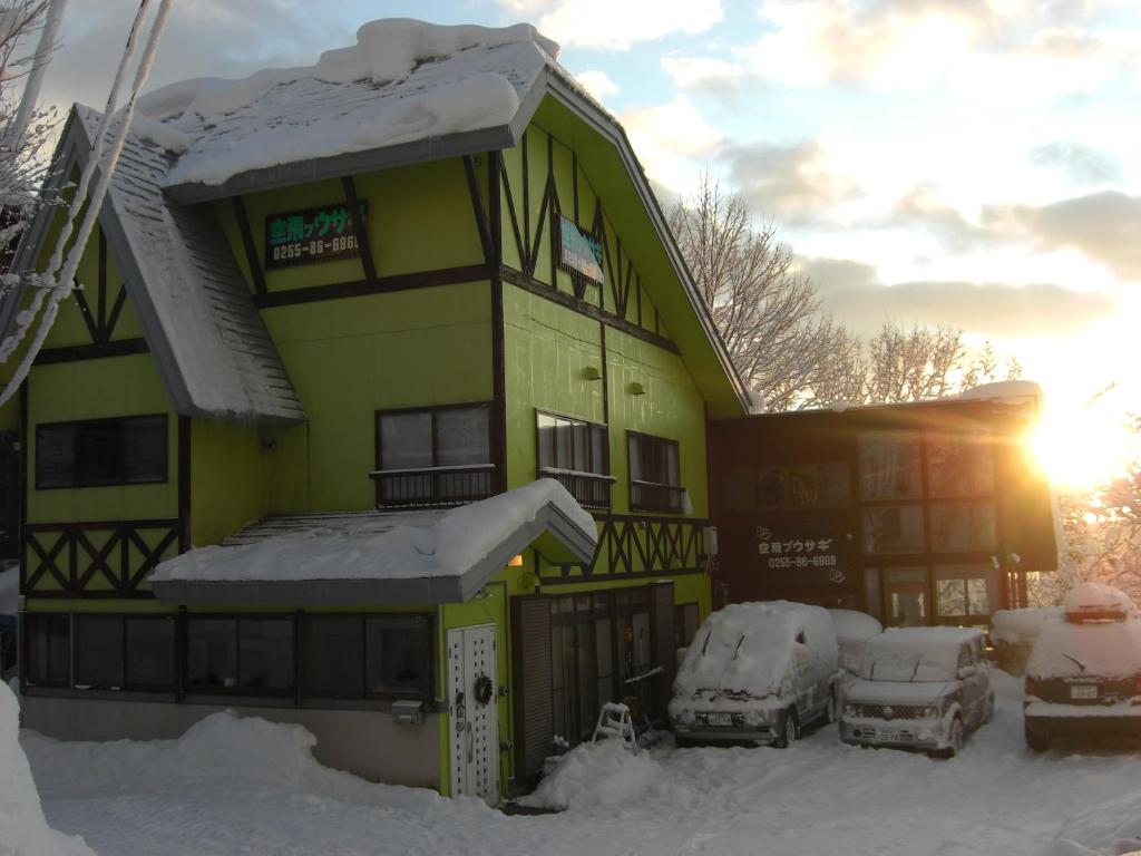 a snow covered house with cars parked in front of it at Soratobu Usagi in Myoko