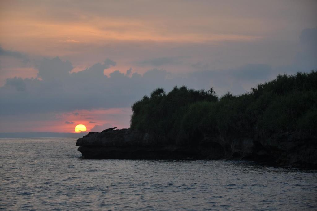 a sunset over a small island in the water at Dream Beach Huts in Nusa Lembongan