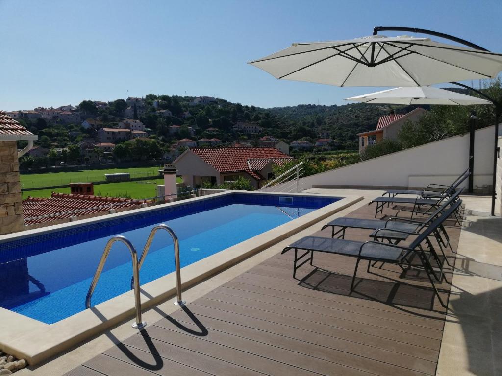 een zwembad met 2 stoelen en een parasol bij Apartments Ivana in Postira