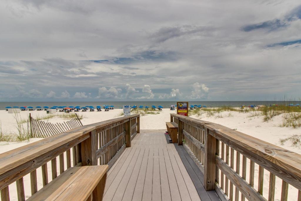 una passerella di legno che conduce alla spiaggia con ombrelloni di Romar Beach Condos a Gulf Shores