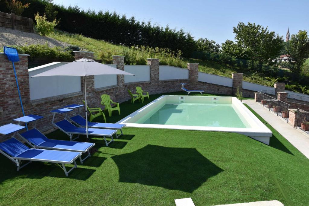una piscina con sillas de césped y sombrilla en B&B La Dolce Vita, en Priocca