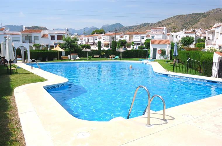 uma grande piscina azul com edifícios ao fundo em B&B Nerja em Nerja