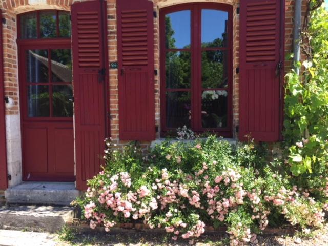 a building with red doors and a bush of flowers at La Maison aux Volets Rouges in La Ferté-Beauharnais