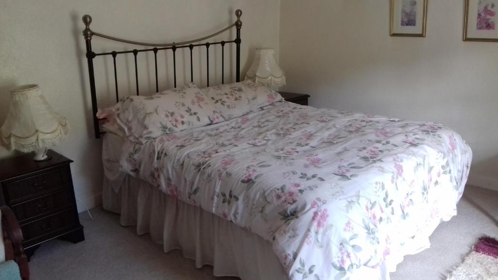 a bedroom with a bed with a floral comforter and two lamps at Hills Farm B&B Laugharne in Laugharne