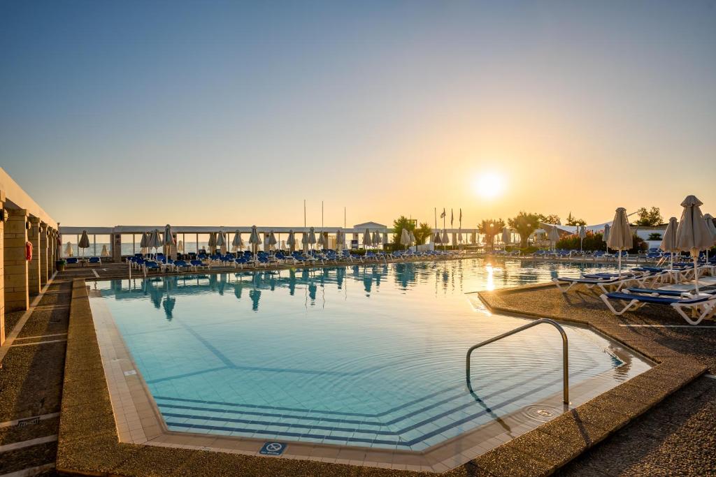a large swimming pool with chairs and the sun setting at Annabelle Beach Resort in Hersonissos