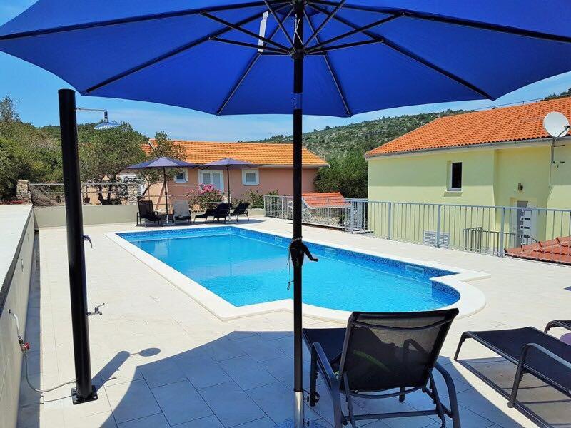 a blue umbrella and a chair next to a swimming pool at Villa 4 Princesses in Vela Luka