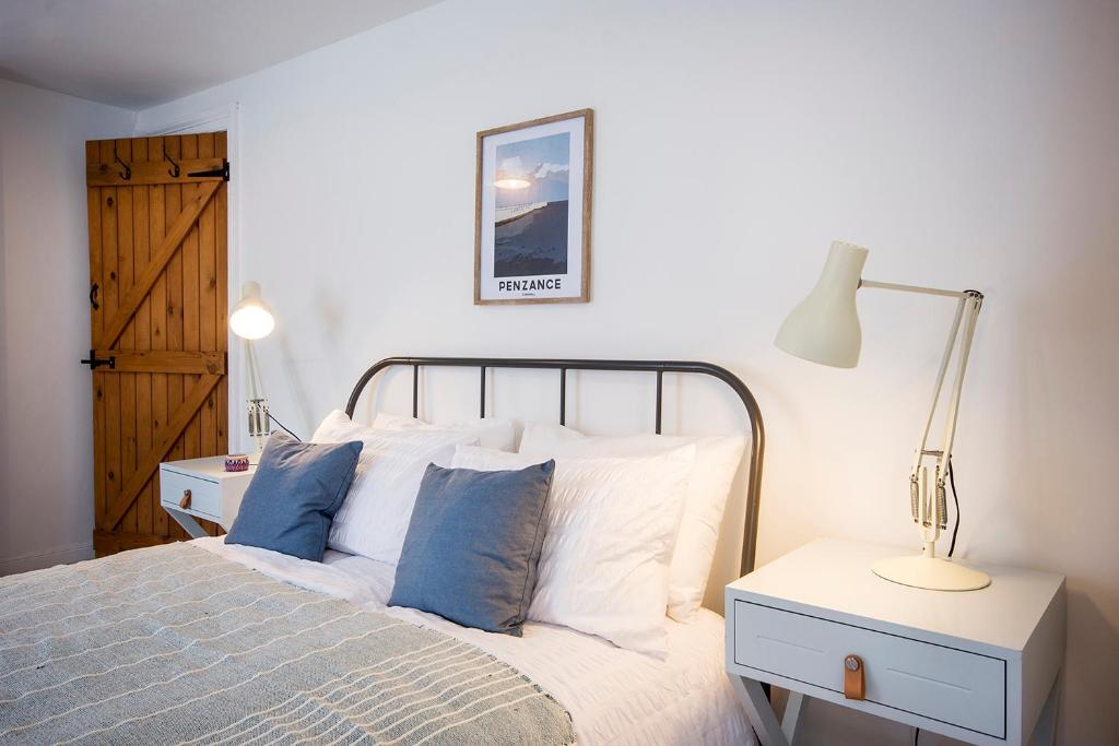 a bedroom with a bed with white sheets and blue pillows at Cornish Cottage - Truro City Centre in Truro