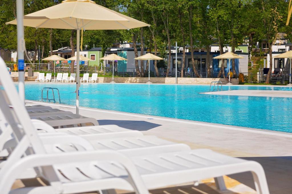 uma piscina com espreguiçadeiras brancas e um guarda-sol em Caravans Bijela Uvala em Poreč