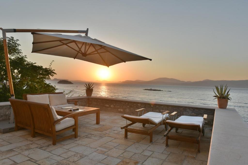 eine Terrasse mit einem Tisch, Stühlen und einem Sonnenschirm in der Unterkunft Hydra Kamini Beach Thea in Hydra