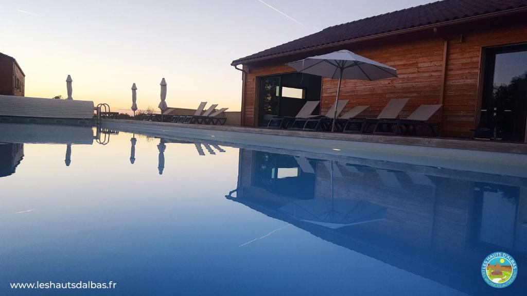 uma piscina com cadeiras e um guarda-sol ao lado de um edifício em Les Hauts d'Albas em Albas