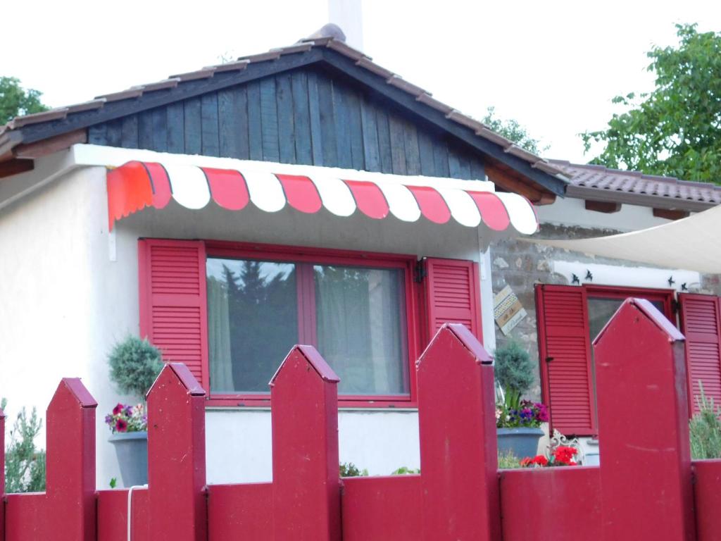 una cerca roja frente a una casa con persianas rojas en 1957 To Rodo kai to Roido, en Karpenisi