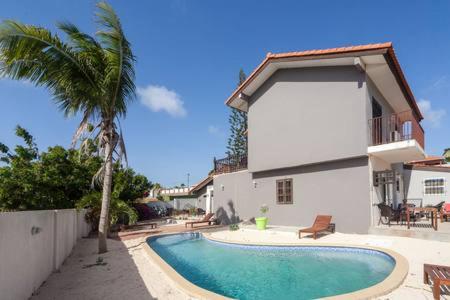 a swimming pool in front of a house with a palm tree at Advantage Apartments Curacao in Willemstad