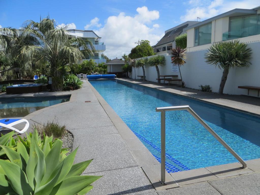 a swimming pool next to a building with palm trees at Cutterscove Resort Apartments in Mount Maunganui