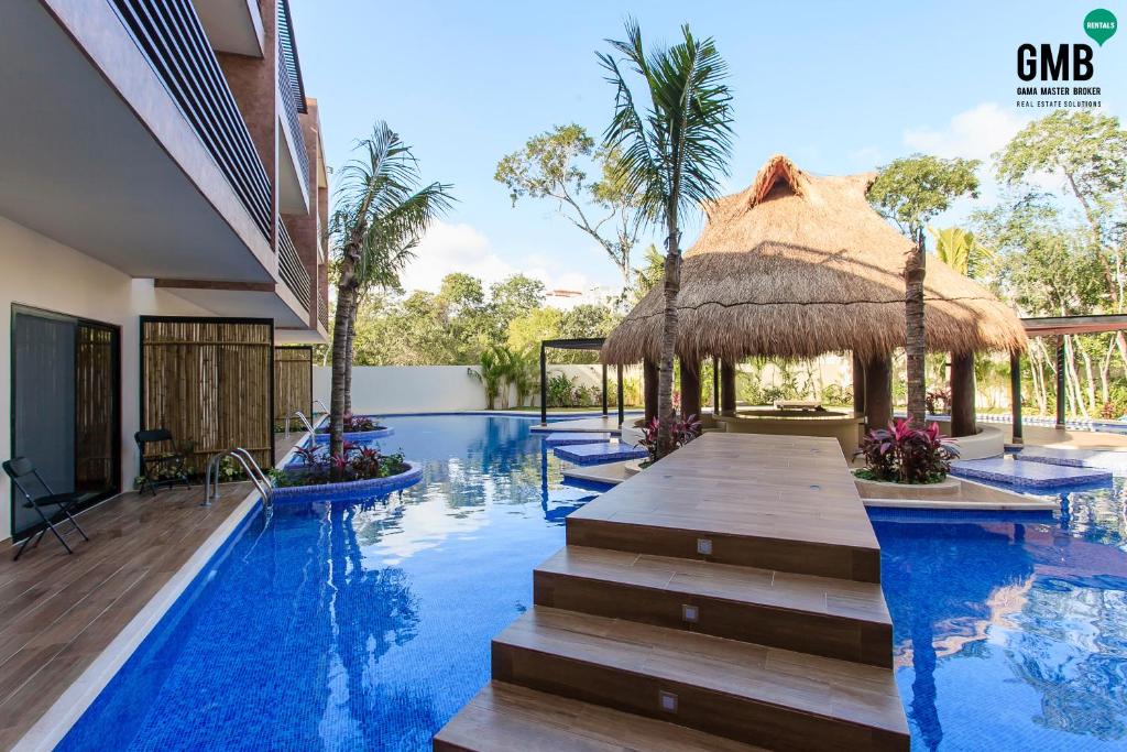 a swimming pool with a straw umbrella and a resort at Magic Paramar Terra C103 in Aldea Zama Tulum in Tulum