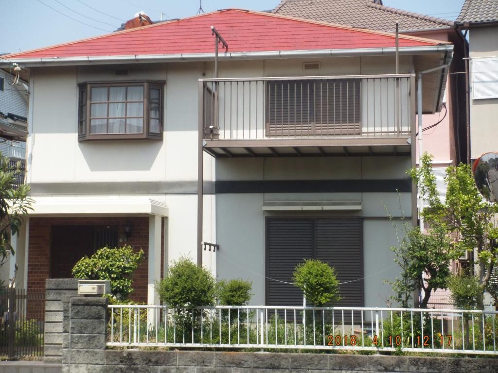 ein Haus mit rotem Dach und einem Zaun in der Unterkunft Hirakata-park Guesthouse in Hirakata