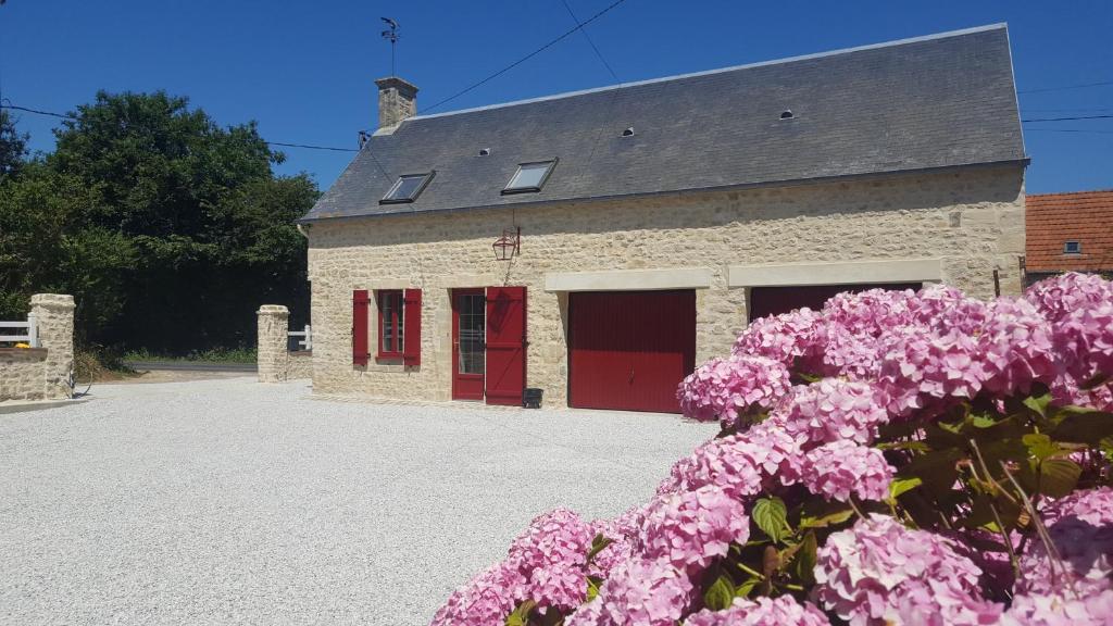 ceglany budynek z czerwonymi drzwiami i różowymi kwiatami w obiekcie gîte de la Girouette w mieście Englesqueville-la-Percée
