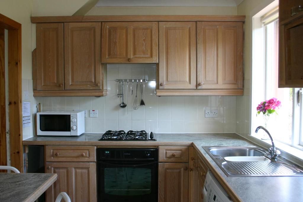 una cucina con armadi in legno, lavandino e forno a microonde di Garden Cottage a Prestwick