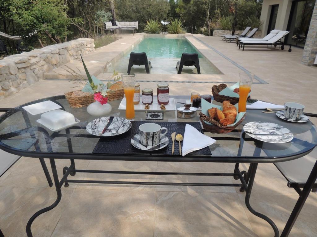 a glass table with food on it next to a pool at La Villa Kallisté in Vacquières