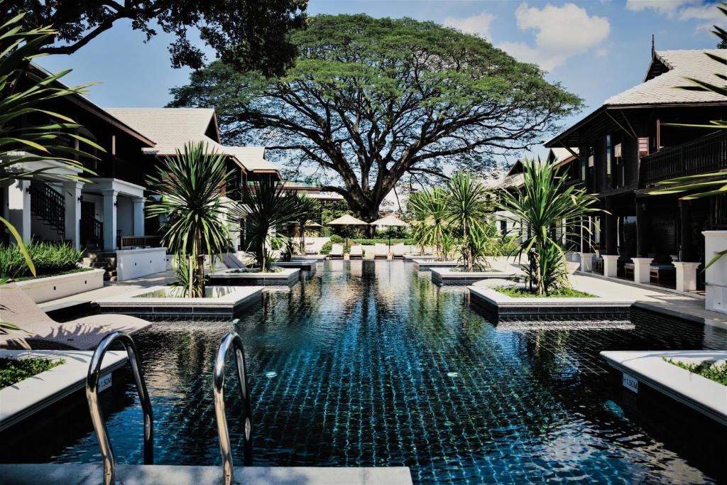 a large swimming pool with a large tree in front of it at Na Nirand Romantic Boutique Resort in Chiang Mai