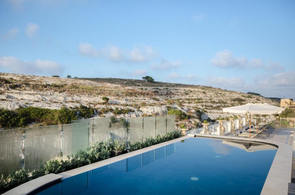 a swimming pool with a hill in the background at Cesca's Boutique Hotel in Xlendi