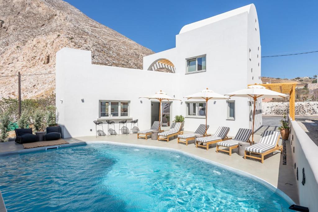 una piscina frente a una casa blanca con sillas y sombrillas en Aegean Gem en Kamari