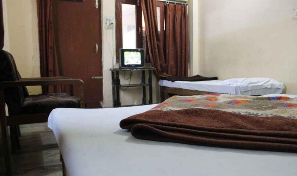 a room with a bed and a chair and a television at Hotel Vardaan in Kankhal