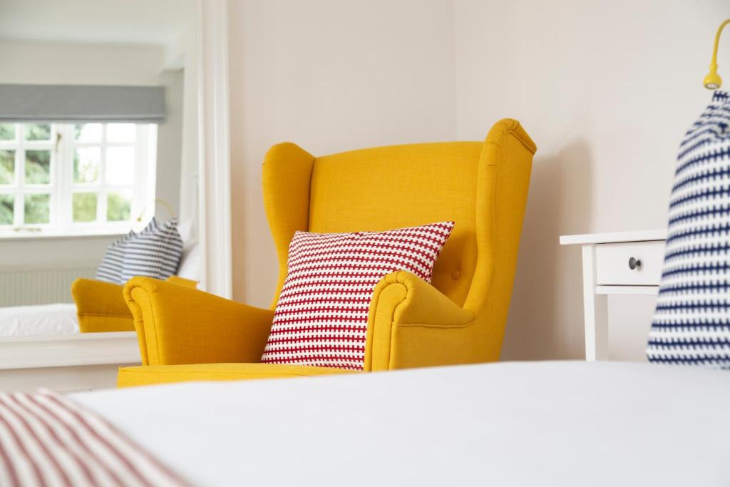a yellow chair with a red and white pillow in a bedroom at Five Bells Inn, Wrentham in Wrentham