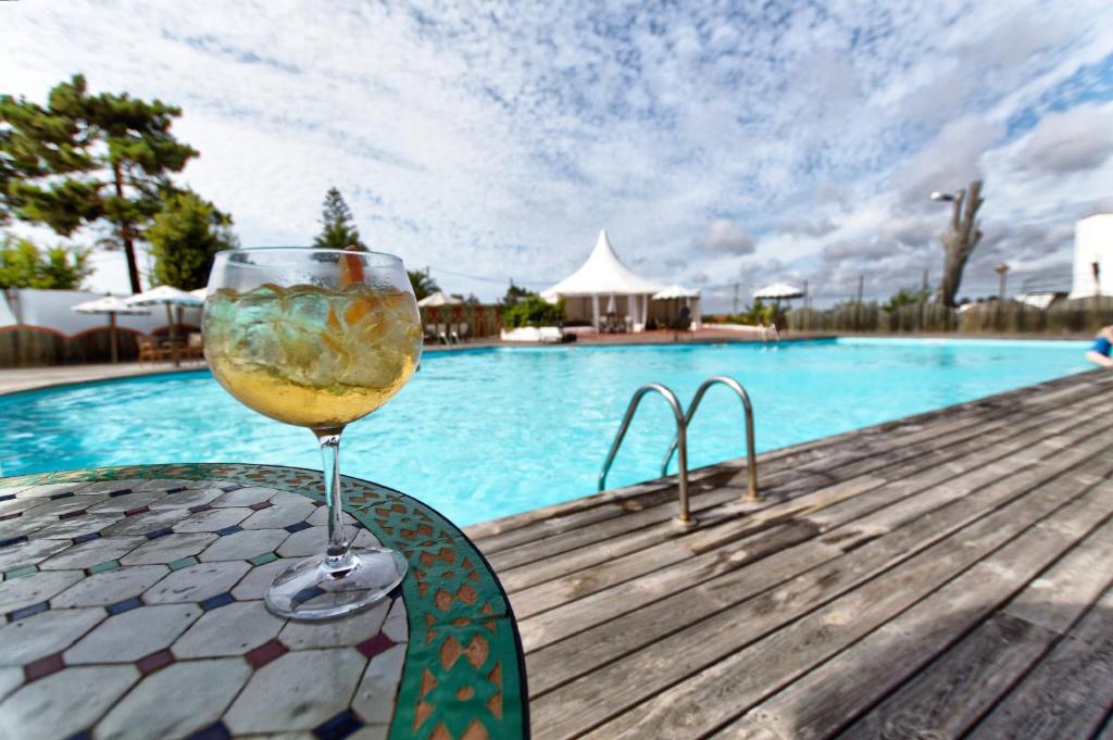 a glass of wine sitting on a table next to a pool at Hotel Vale Da Telha in Aljezur