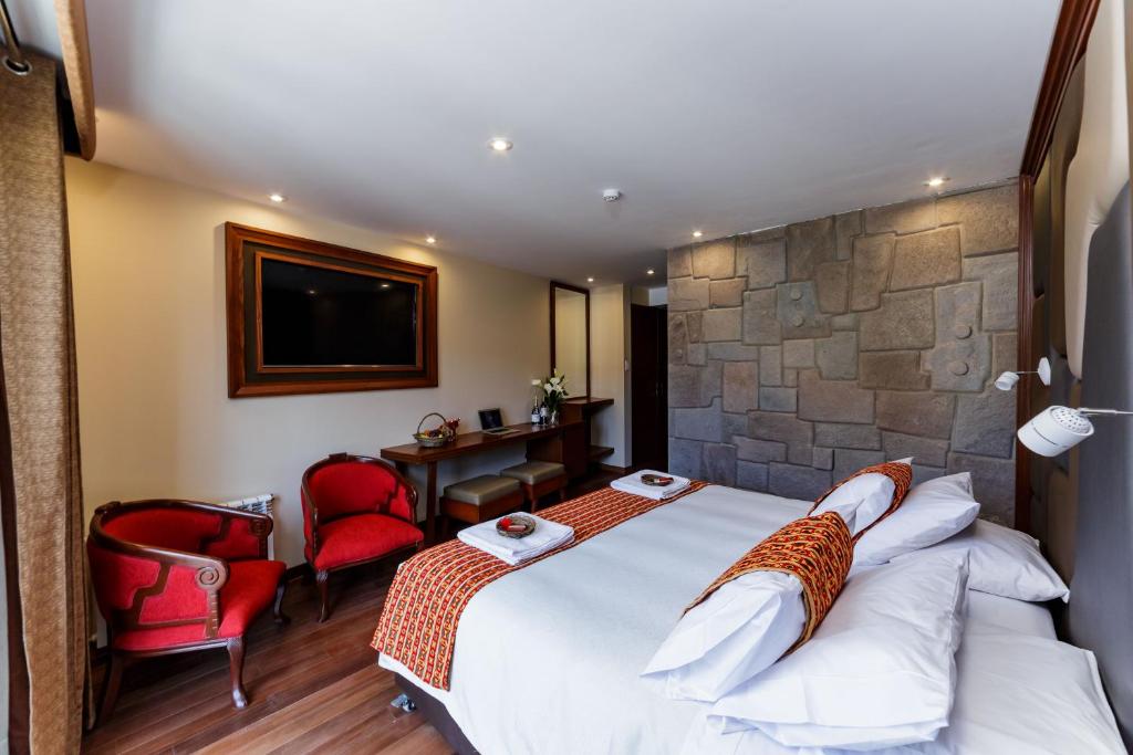 una habitación de hotel con una cama grande y sillas rojas en Yawar Inka Hotel, en Cusco