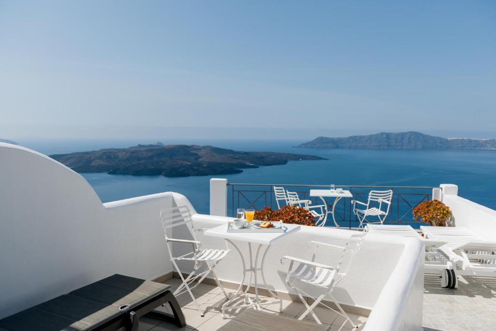 a balcony with white tables and chairs and the ocean at Villa Renos Hotel in Fira