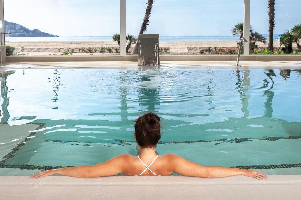 a woman laying in a swimming pool looking at the ocean at Hotel Montecarlo Spa & Wellness in Roses