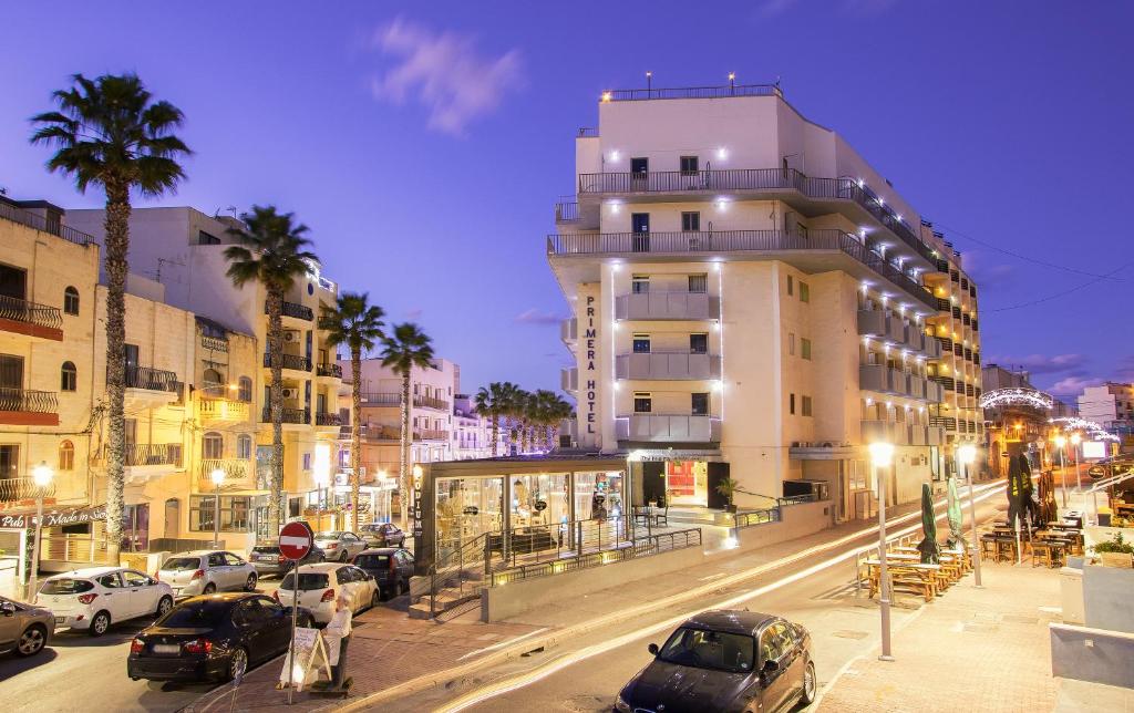 una strada cittadina con auto parcheggiate di fronte a un edificio di Primera Hotel a San Pawl il-Baħar