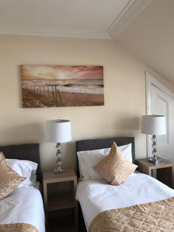 two beds in a bedroom with two lamps and a painting at Royal Guest House Nairn in Nairn