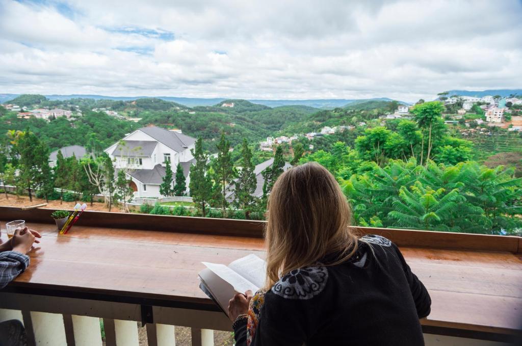 kobieta czytająca książkę na balkonie domu w obiekcie Tigon Dalat Hostel w mieście Da Lat