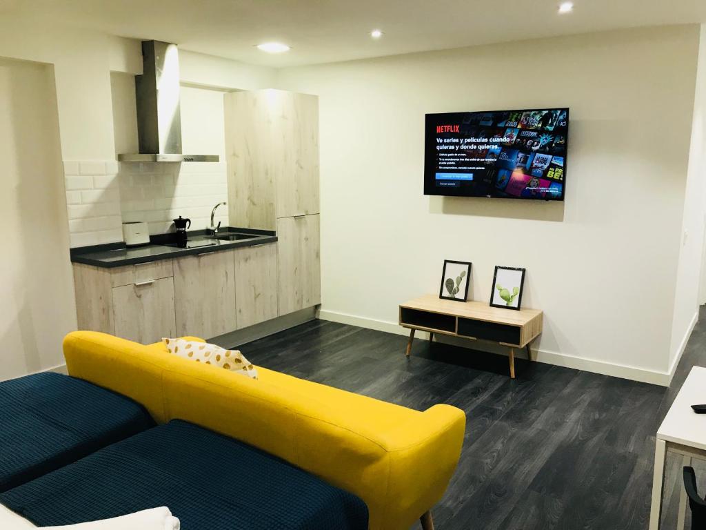 sala de estar con sofá amarillo y TV en Apartamentos Arriba by gaiarooms, en Salamanca