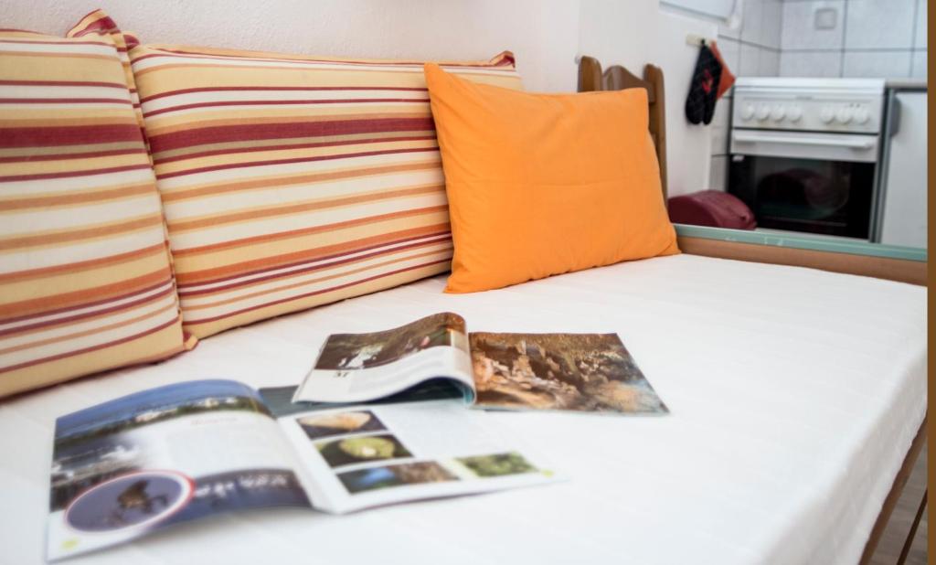 a bed with an open book on it with an orange pillow at Seaview Aparthotel in Nea Potidaea