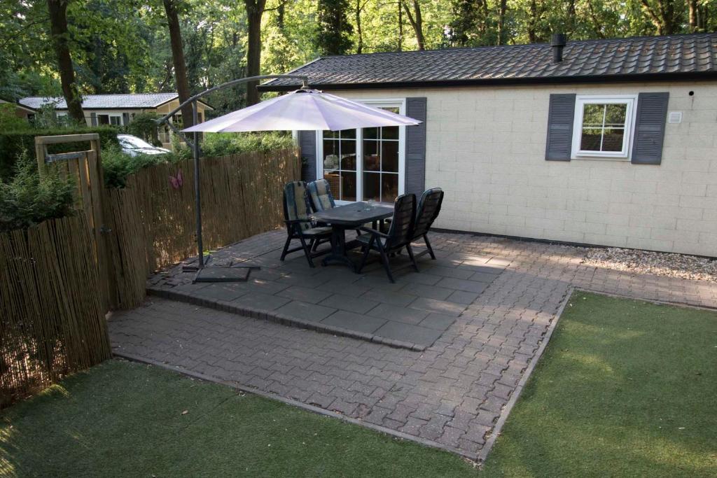 un patio con mesa, sillas y sombrilla en Chalet Vakantie Wageningen Veluwe en Wageningen