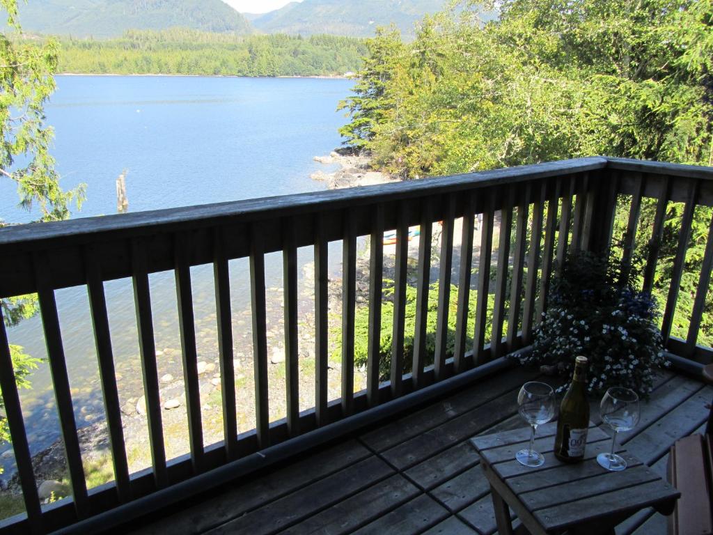 a deck with a view of a lake and a table with wine glasses at 203 at Water's Edge in Ucluelet