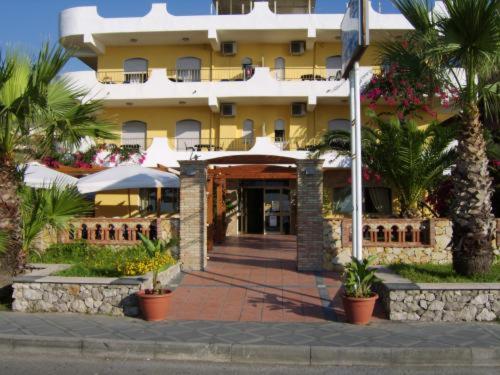 a large yellow building with palm trees in front of it at Hotel Solemar in SantʼAlessio Siculo