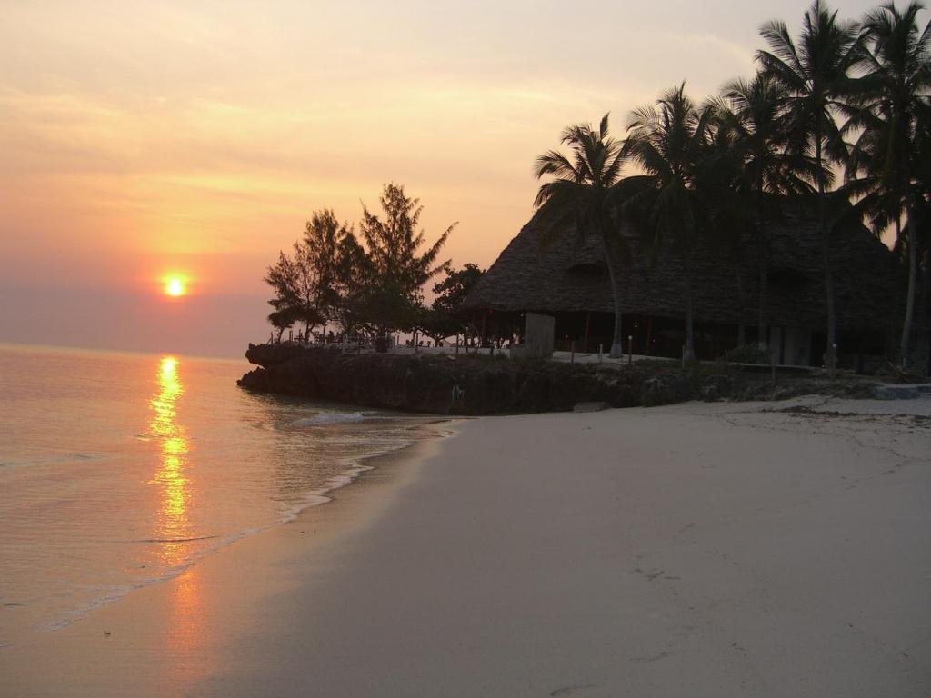 a beach with a house and palm trees at sunset at Karamba Eco Boutique Hotel in Kizimkazi