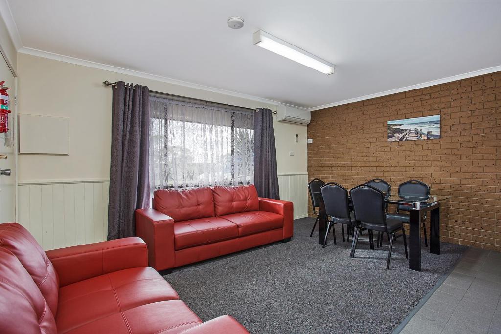 sala de estar con sofá rojo, mesa y sillas en Warrnambool Motel and Holiday Park en Warrnambool