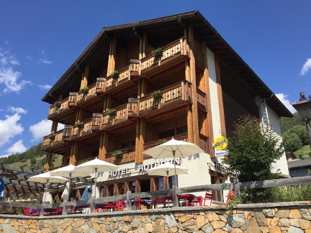 a large building with tables and umbrellas in front of it at Hotel Restaurant Rothorn in Visperterminen